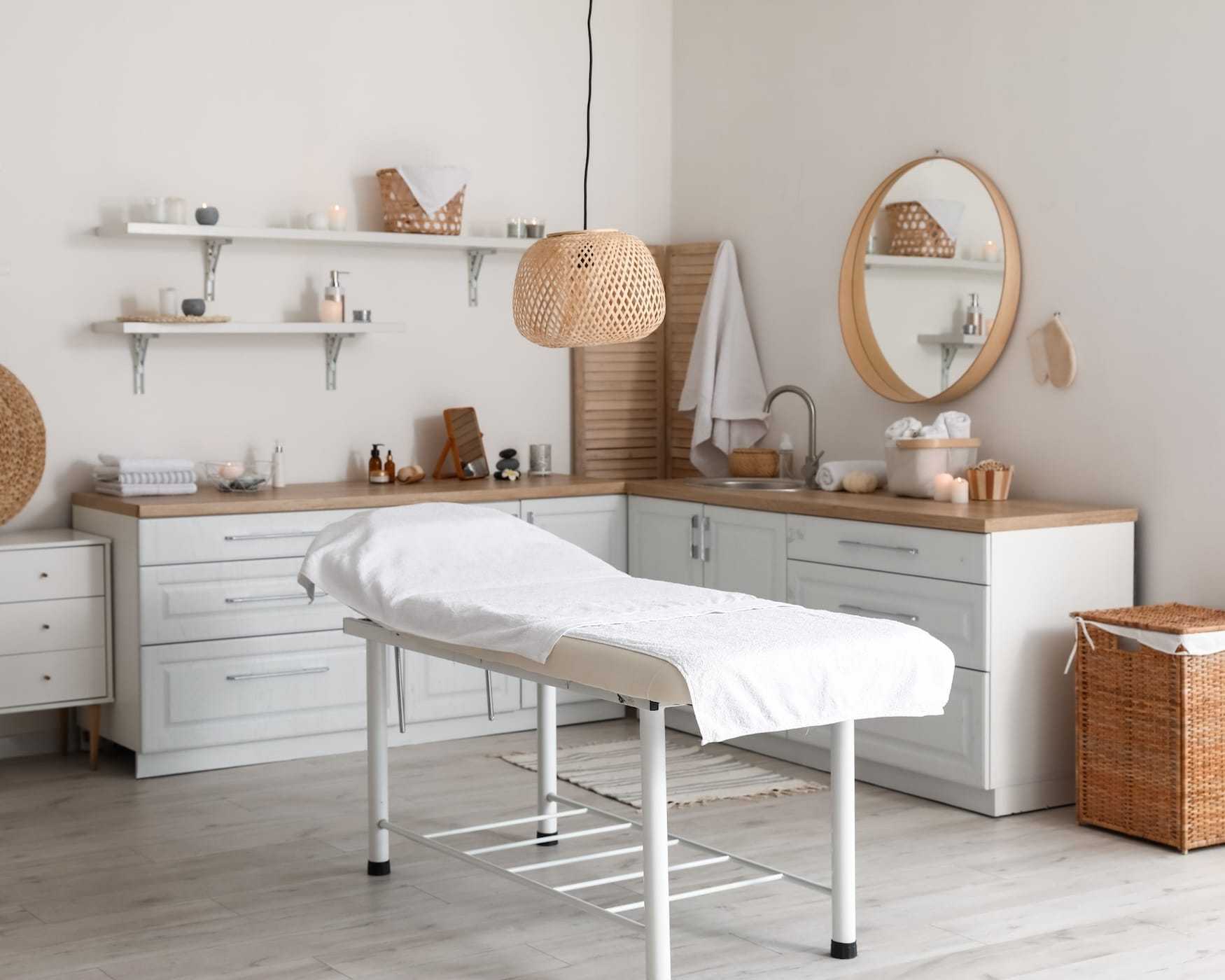 Minimalist spa room with a massage table, white cabinets, and serene decor.