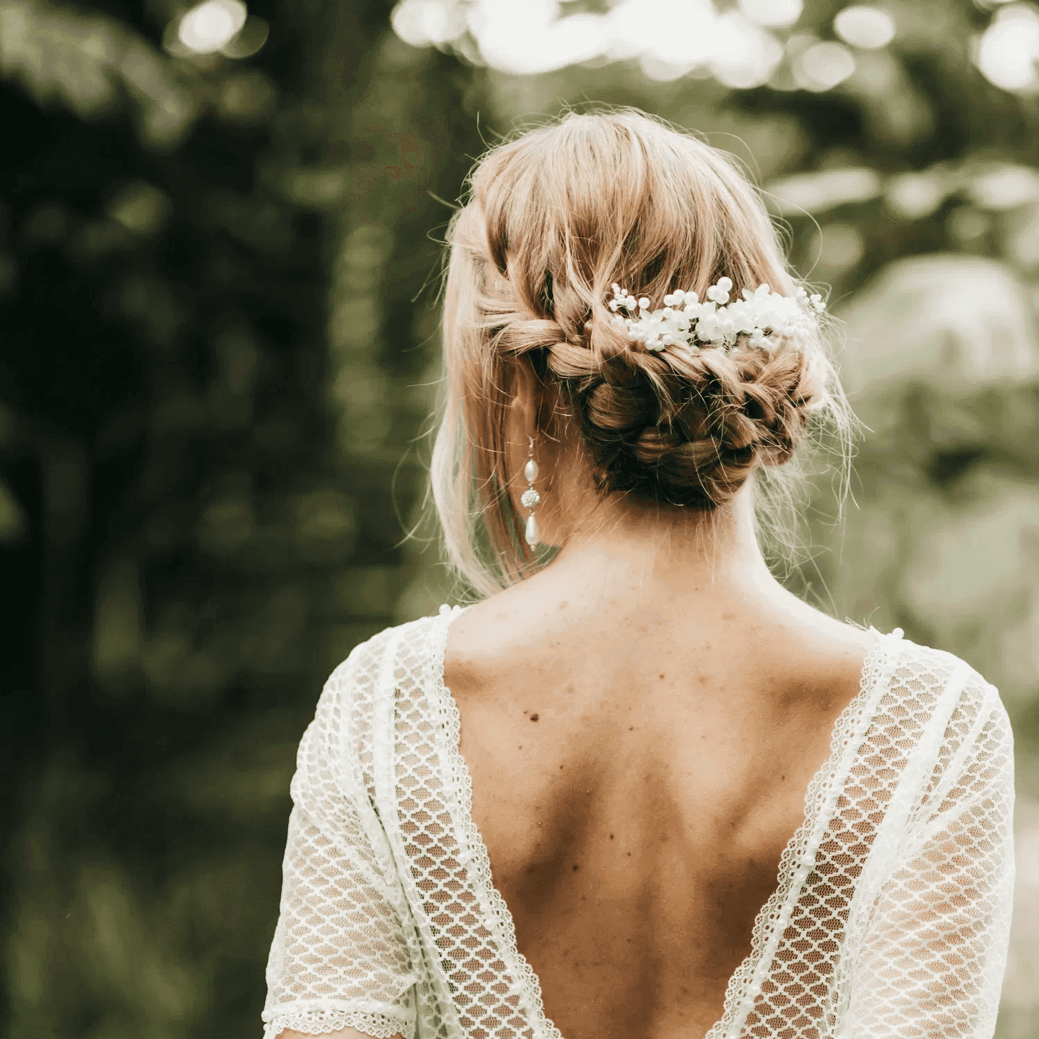 Bride in lace dress with floral hairpiece, back view in lush garden.