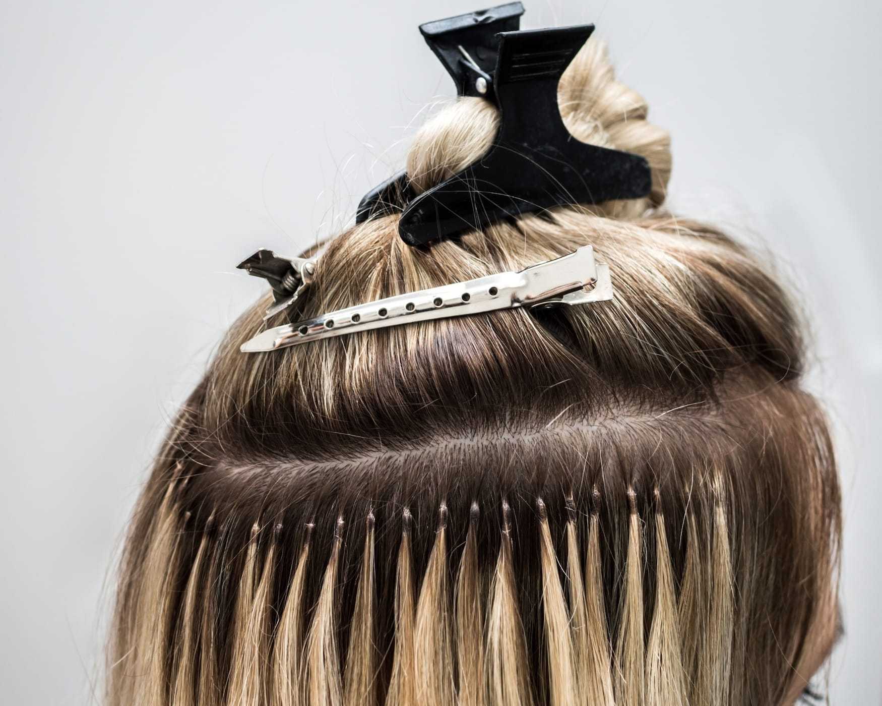 Hair extensions being applied with clips and beads on a woman's head, showing the process close-up.