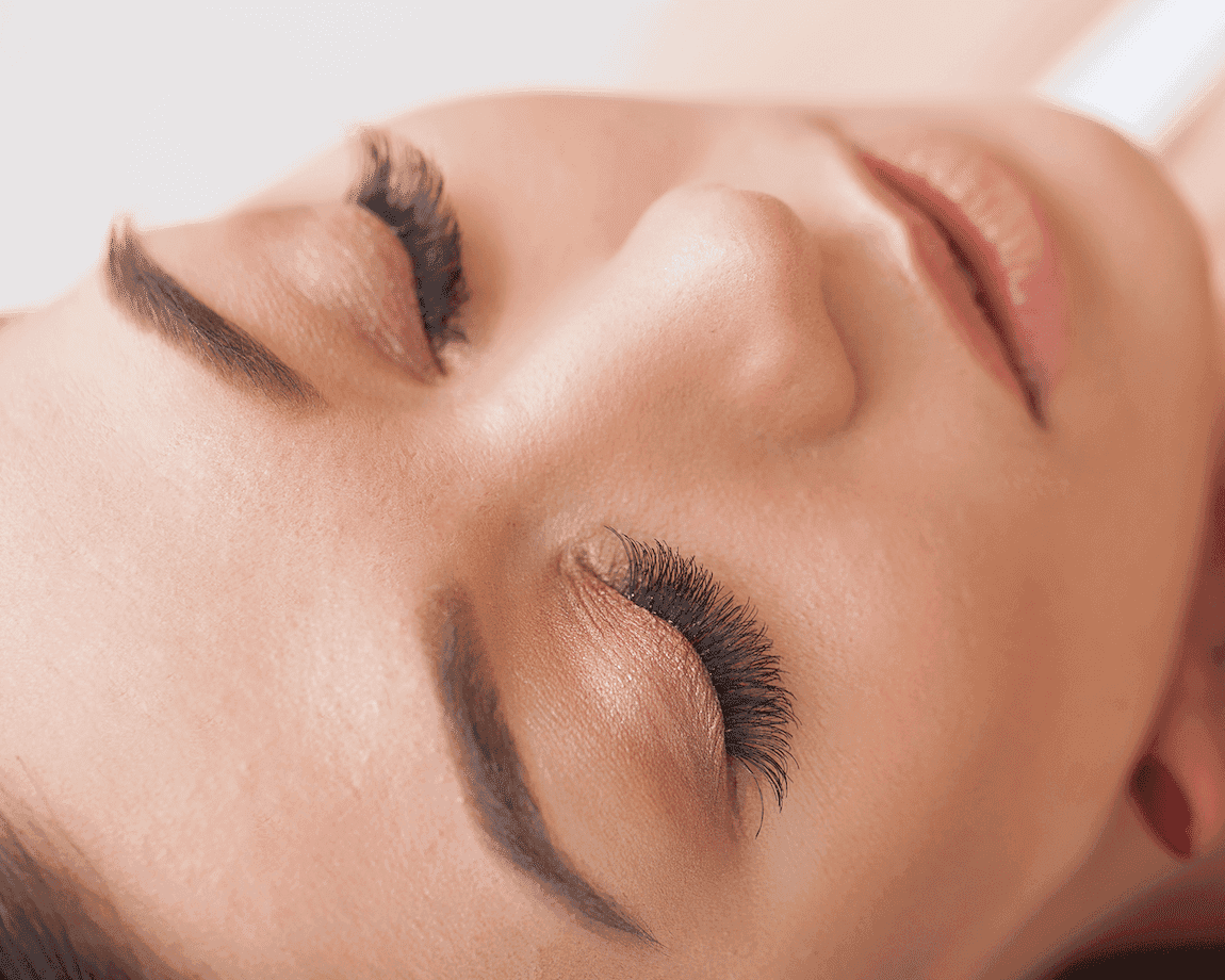 Close-up of a woman's face with closed eyes showing long, thick eyelashes and smooth skin.